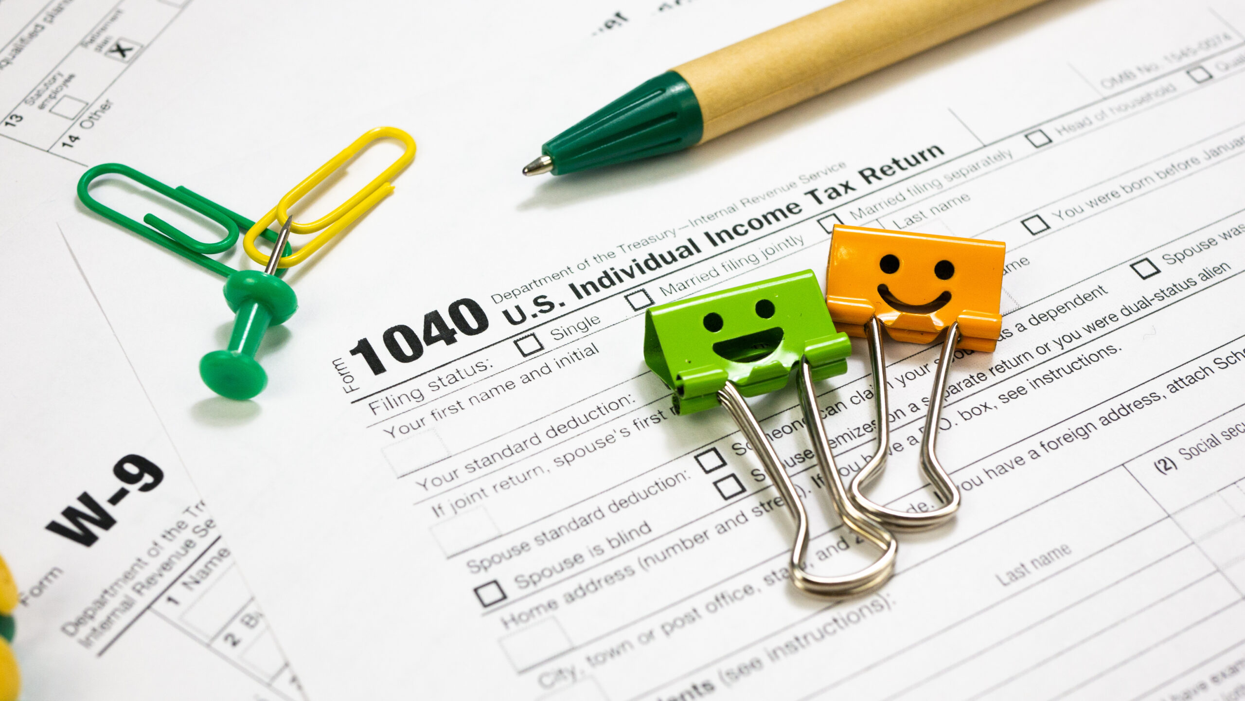 IRS 1040 and W-9 U.S. Tax Forms with smile binder clips, pen and clips. Wage statement and tax time concept